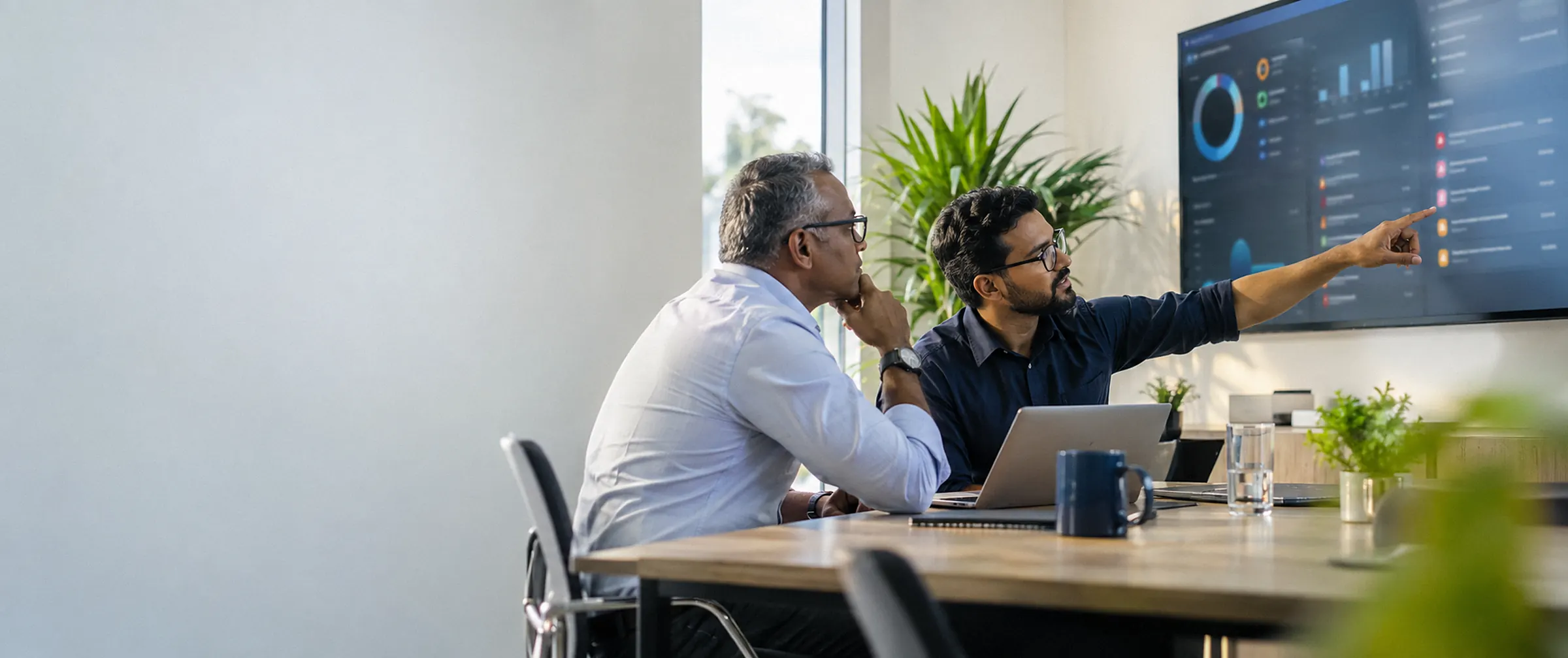 Two consultants reviewing a cloud configuration dashboard on a wall screen, one pointing at a warning